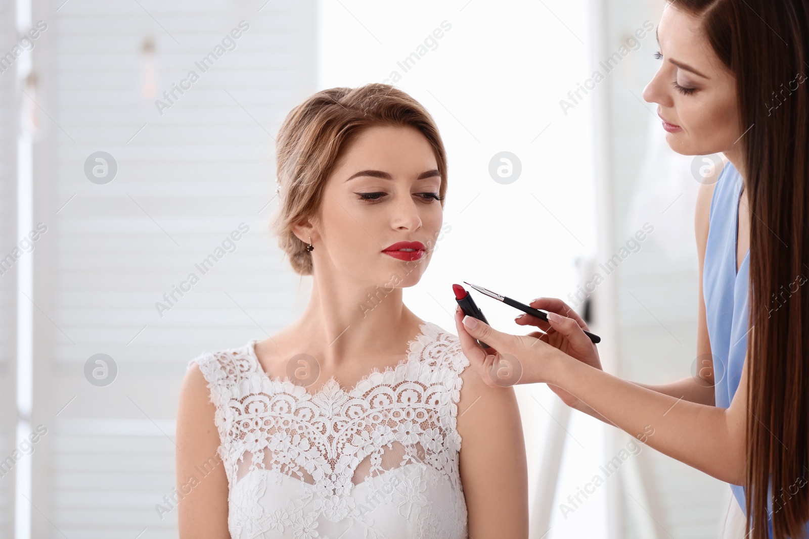 Photo of Makeup artist preparing bride before her wedding in room