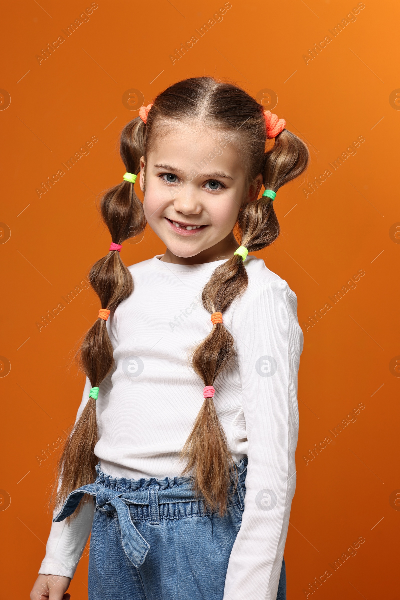 Photo of Cute little girl with beautiful hairstyle on orange background