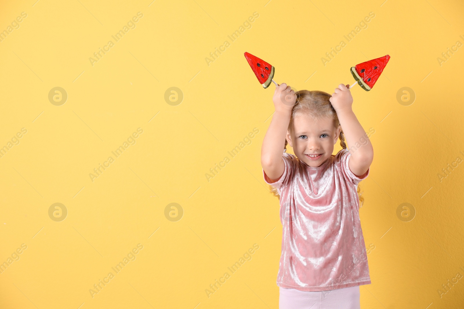 Photo of Cute little girl with candies on color background. Space for text