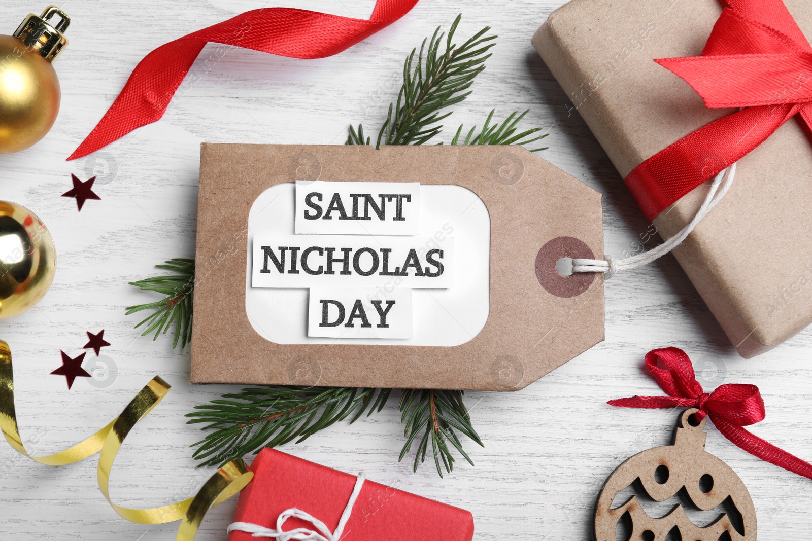 Photo of Tag with text Saint Nicholas Day and festive decor on white wooden table, flat lay