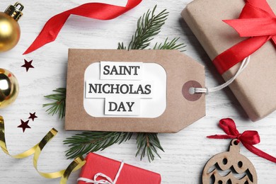 Photo of Tag with text Saint Nicholas Day and festive decor on white wooden table, flat lay