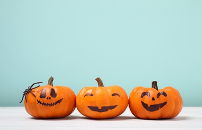 Photo of Pumpkins with scary faces on light turquoise background, space for text. Halloween decor
