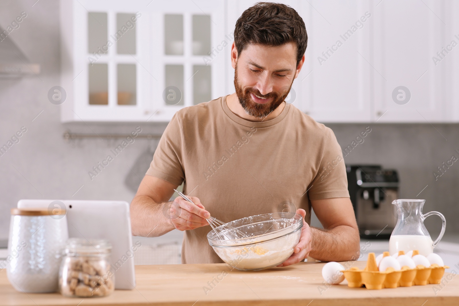 Photo of Man making dough while watching online cooking course via tablet in kitchen