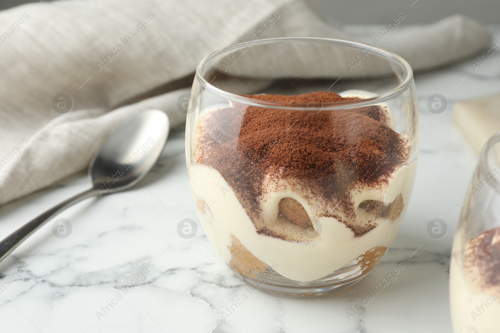 Photo of Delicious tiramisu in glass and spoon on white marble table, closeup