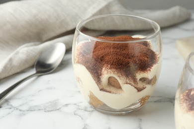 Delicious tiramisu in glass and spoon on white marble table, closeup