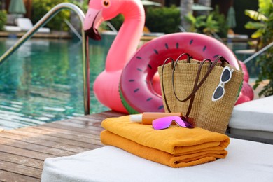 Photo of Beach accessories on sun lounger, inflatable ring and float near outdoor swimming pool. Luxury resort