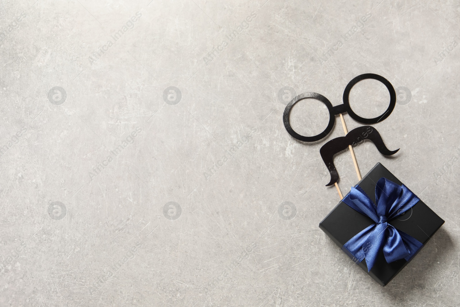 Photo of Gift box, paper glasses and mustache on light grey stone background, flat lay with space for text. Father's day celebration