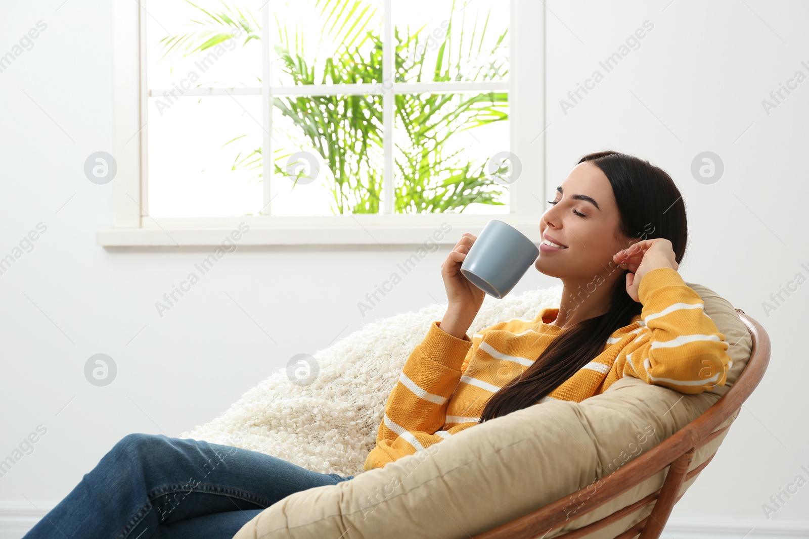 Photo of Young woman relaxing in papasan chair near window at home