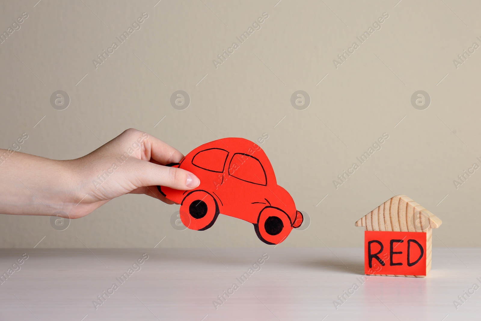 Photo of Woman holding red car near wooden house at white table, closeup. ABA therapy concept