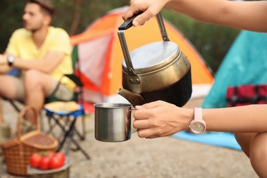 Photo of Woman pouring water into mug near camping tent outdoors, closeup