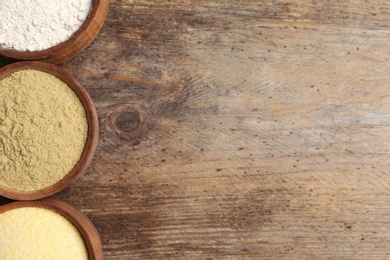 Bowls with different types of flour on wooden background, top view. Space for text