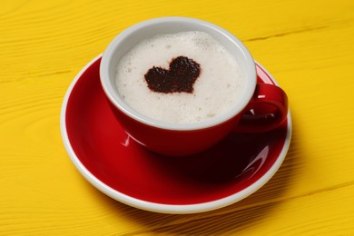Cup of aromatic coffee with heart shaped decoration on yellow wooden table