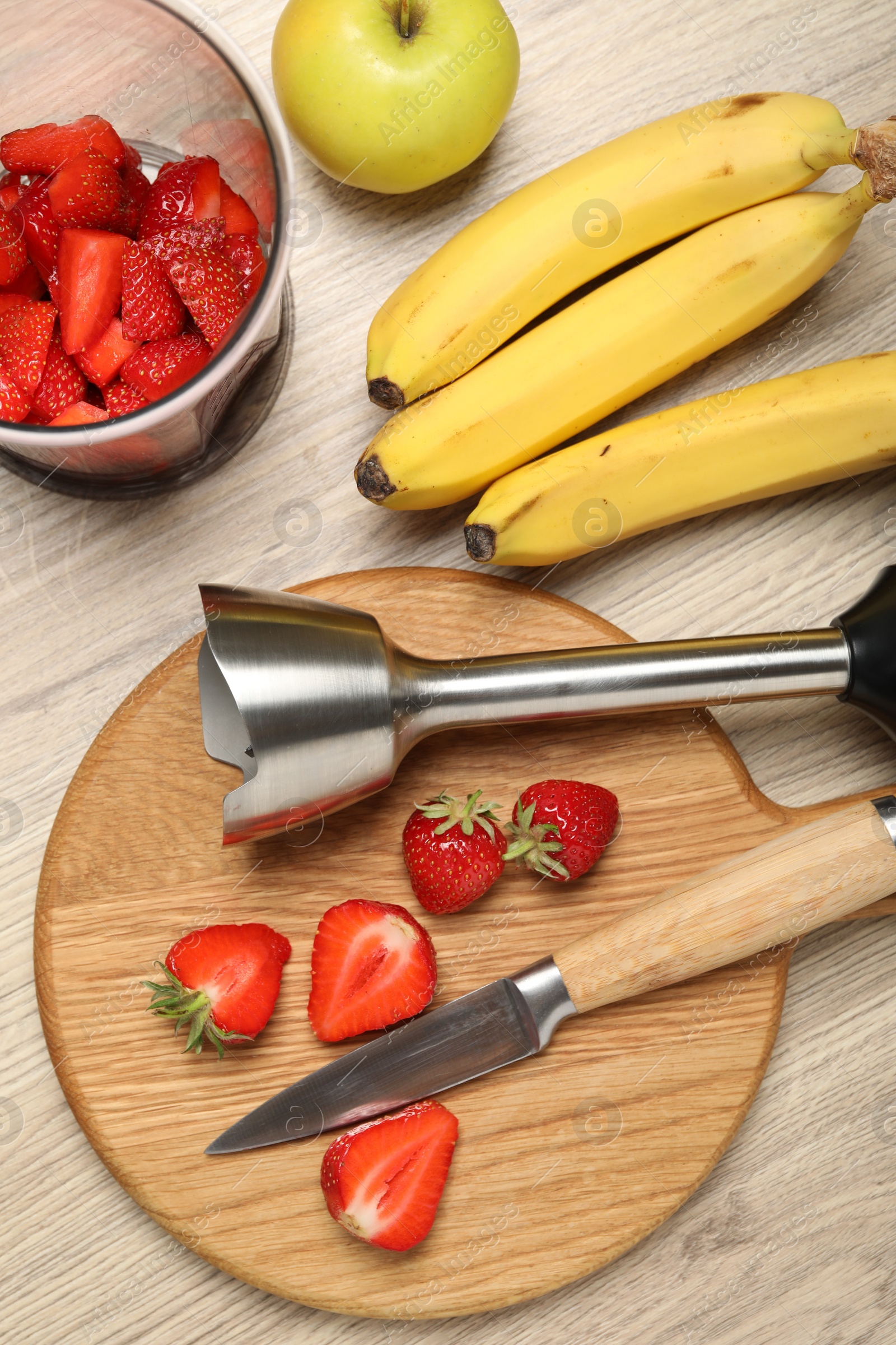 Photo of Hand blender kit, fresh fruits, strawberries and knife on wooden table, flat lay