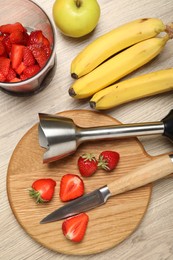 Photo of Hand blender kit, fresh fruits, strawberries and knife on wooden table, flat lay