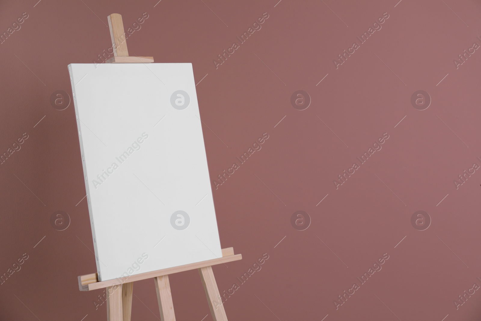Photo of Wooden easel with blank canvas on dusty rose background. Space for text