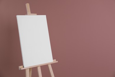 Photo of Wooden easel with blank canvas on dusty rose background. Space for text