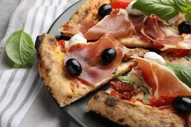 Photo of Tasty pizza with cured ham, olives, mozzarella cheese, sun-dried tomato and basil on table, closeup