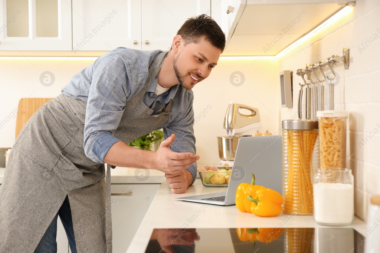 Photo of Man making dinner while watching online cooking course via laptop in kitchen