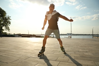 Handsome young man roller skating on pier near river