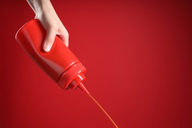 Woman pouring tasty ketchup from bottle on red background, closeup. Space for text