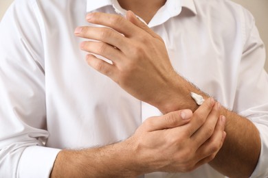 Photo of Man applying cream onto hand on beige background, closeup