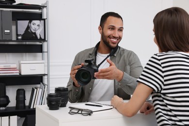 Young professional photographer holding camera while talking with woman in modern photo studio