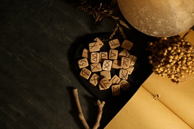 Photo of Wooden runes and dried flowers on black marble table, flat lay. Space for text