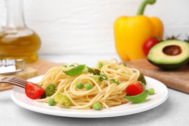 Plate of delicious pasta primavera and ingredients on light gray table, closeup