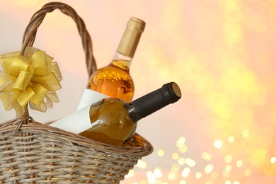 Photo of Wicker basket with bottles of wine against blurred lights, space for text