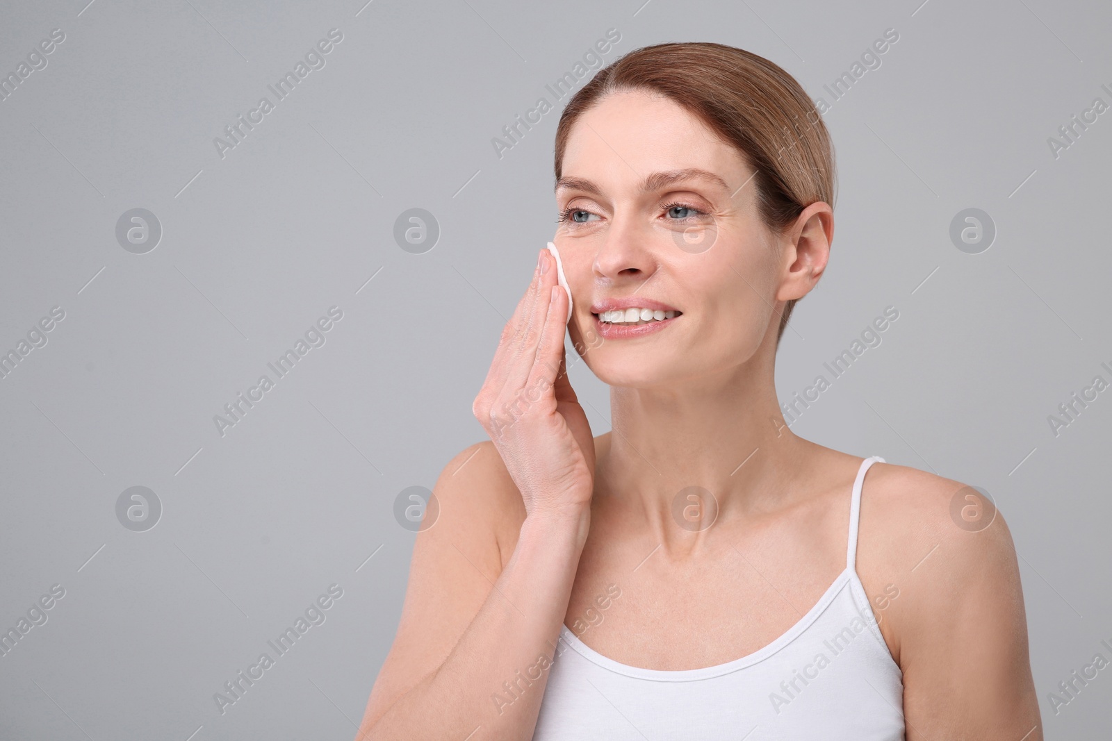 Photo of Beautiful woman removing makeup with cotton pad on gray background, space for text