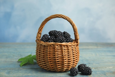 Photo of Wicker basket of tasty blackberries on blue wooden table
