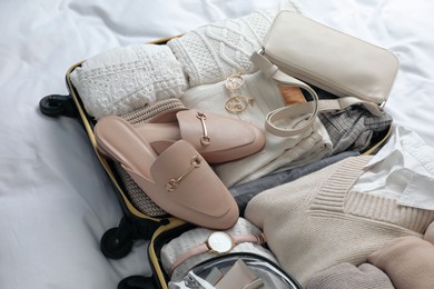 Photo of Open suitcase with folded clothes, shoes and accessories on bed