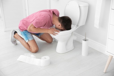 Photo of Young man vomiting in toilet bowl at home