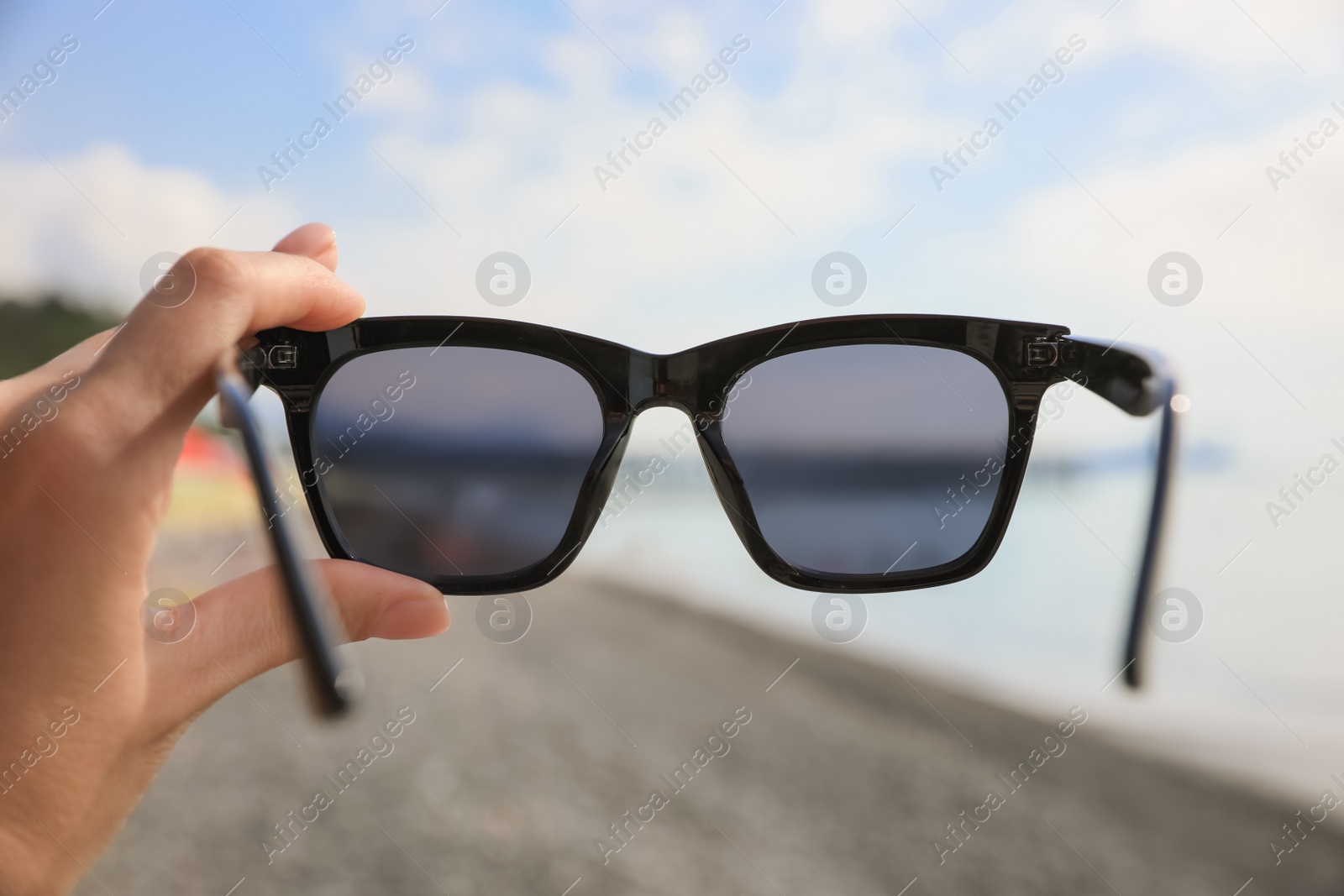 Photo of Woman holding sunglasses near sea on sunny day, closeup