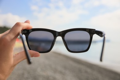 Woman holding sunglasses near sea on sunny day, closeup