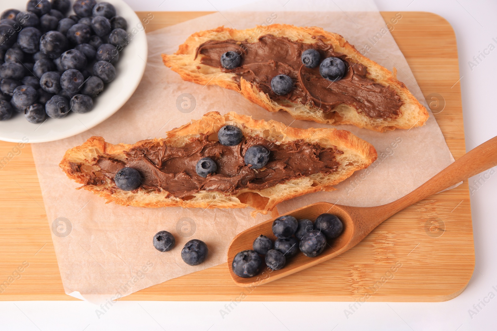 Photo of Tasty croissant with chocolate paste and blueberries on white background, above view