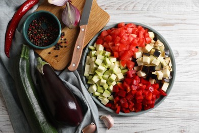 Cooking delicious ratatouille. Fresh ripe vegetables, plate and knife on white wooden table, flat lay