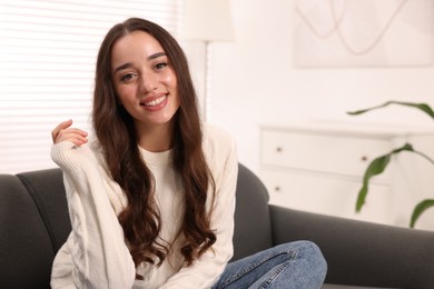 Beautiful young woman in stylish warm sweater on sofa at home, space for text