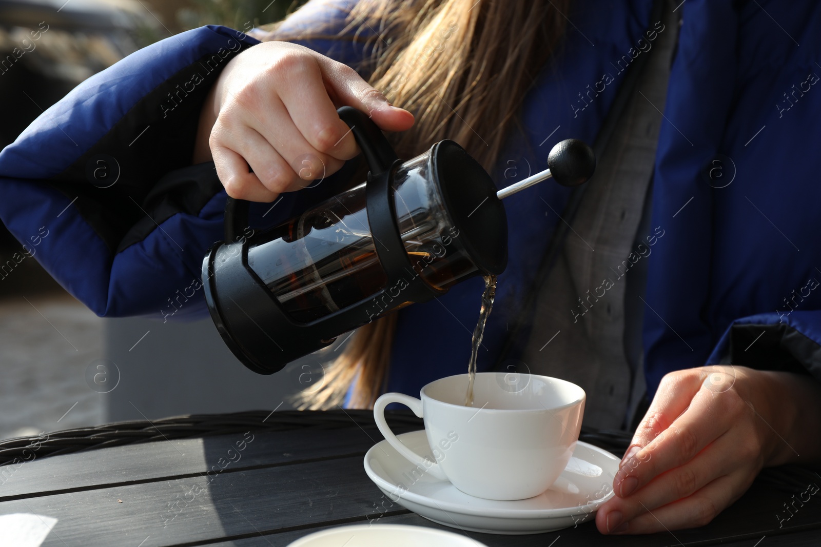 Photo of Woman pouring tea into cup at black wooden table in outdoor cafe, closeup