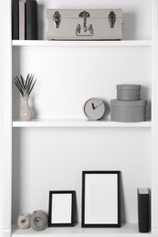 Photo of White shelves with clock, photo frames and different decor indoors. Interior design