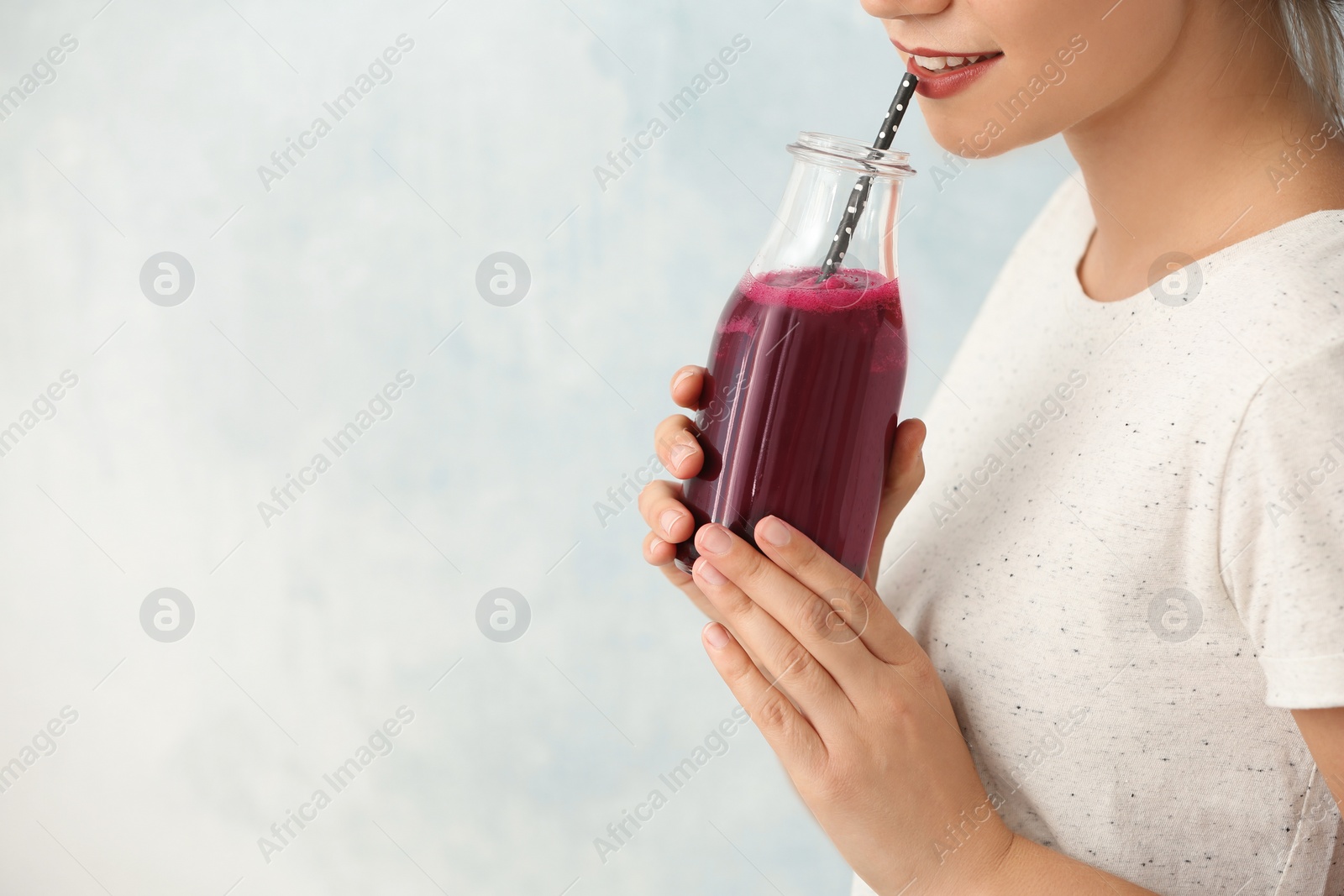 Photo of Woman holding bottle of beet smoothie on light background with space for text, closeup