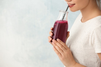 Woman holding bottle of beet smoothie on light background with space for text, closeup