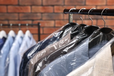 Photo of Dry-cleaning service. Many different clothes hanging on rack against brick wall, closeup