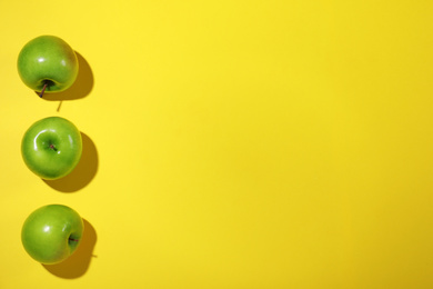 Tasty green apples on yellow background, flat lay. Space for text