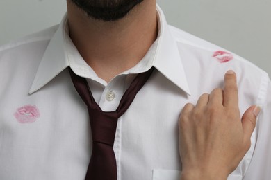 Photo of Woman pointing at lipstick kiss mark on her husband's shirt, closeup