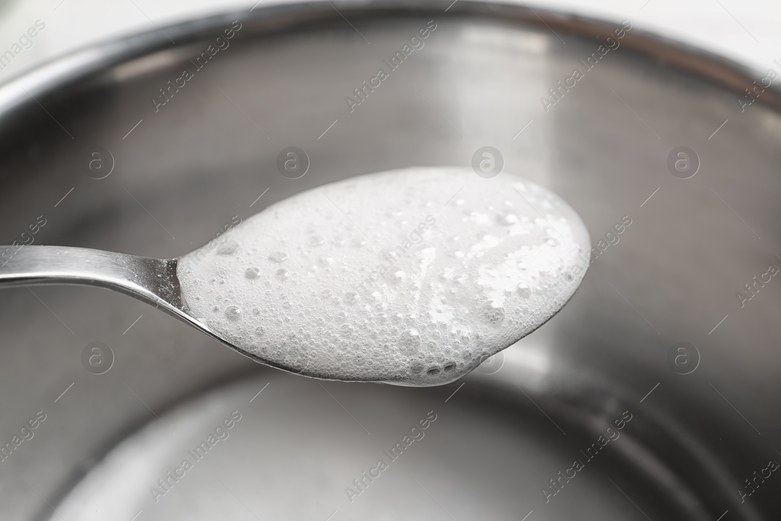 Photo of Chemical reaction of vinegar and baking soda in spoon over saucepan, closeup