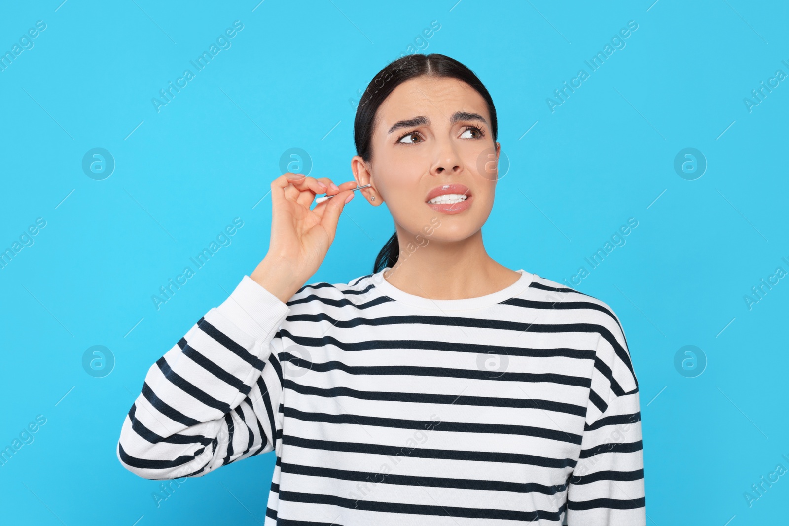 Photo of Young woman cleaning ear with cotton swab on light blue background