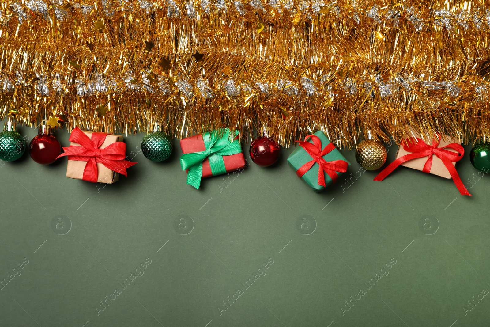Photo of Golden tinsel with Christmas balls and gift boxes on olive background, flat lay. Space for text