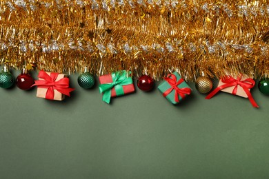 Golden tinsel with Christmas balls and gift boxes on olive background, flat lay. Space for text