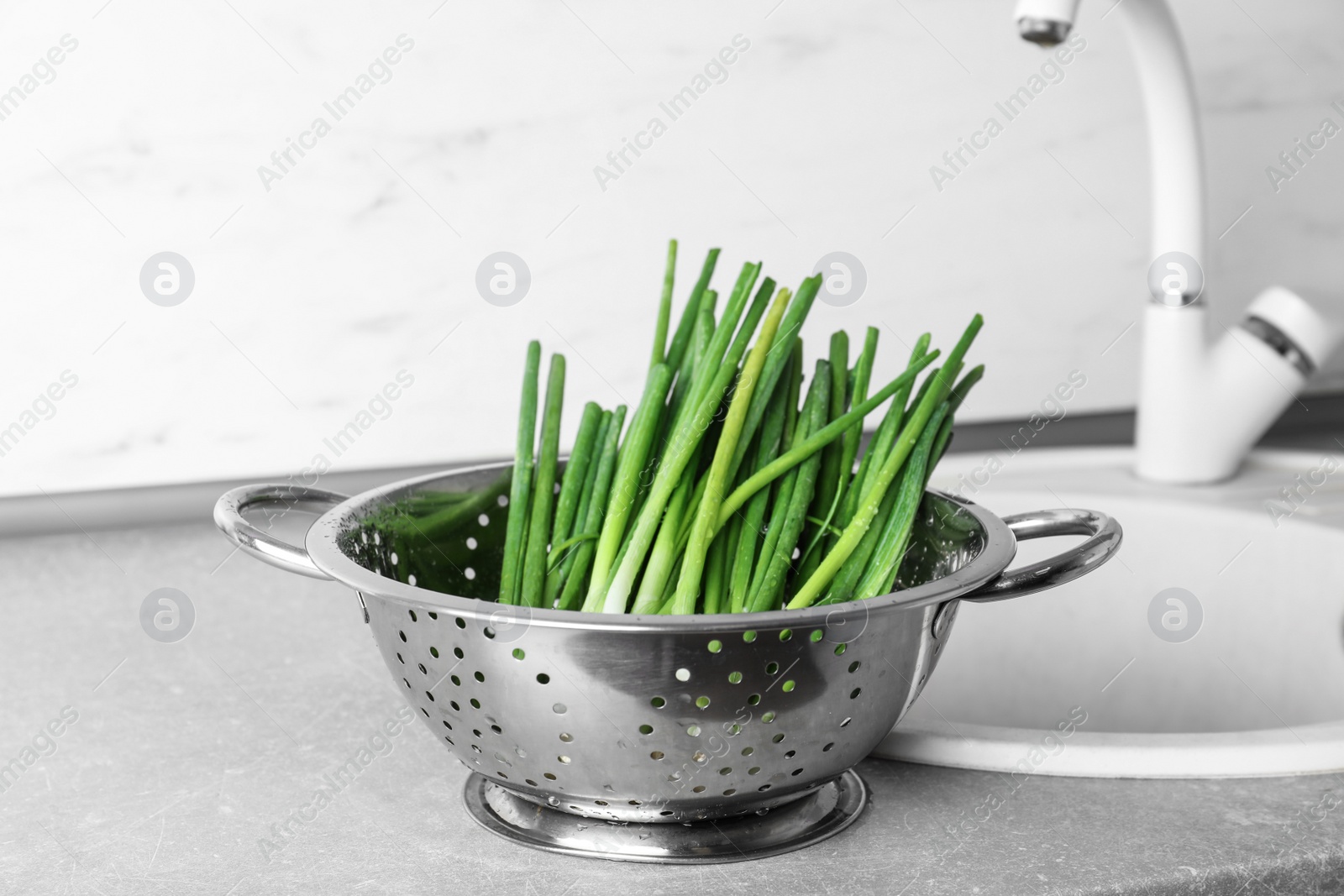 Photo of Colander with bunch of fresh green onions near kitchen sink